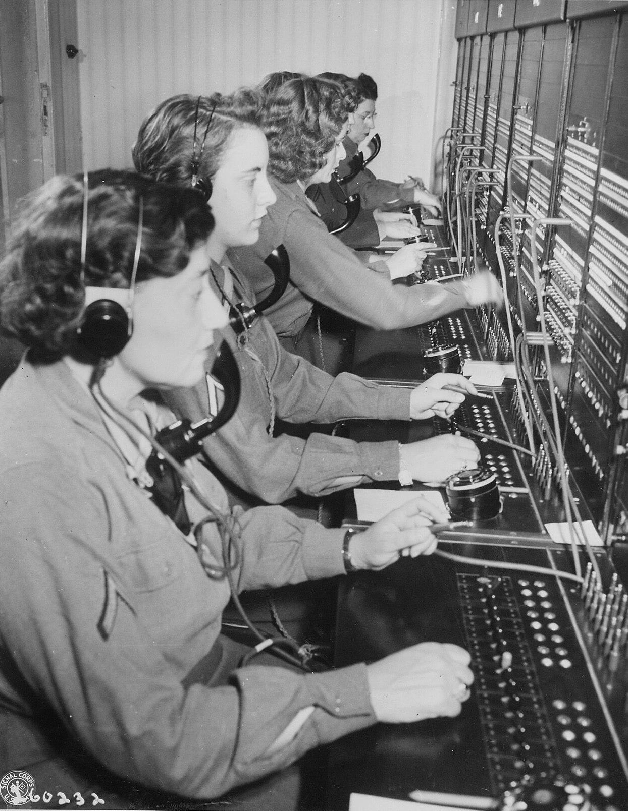 Women's Army Corps operators in headsets work a long switchboard side by side.
